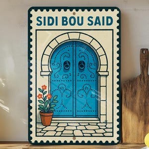May include: Rectangular metal sign featuring a blue door with intricate details, a flower pot, and the text "SIDI BOU SAID." The sign has a vintage stamp design with a cream-colored background and a dark blue border.