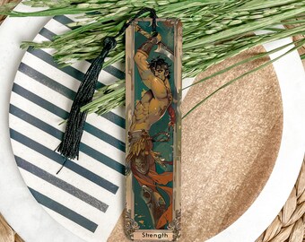 May include: A bookmark featuring a colorful illustration of a muscular figure holding a sword. The background is a green and gold design. The bookmark has the word "Strength" at the bottom.