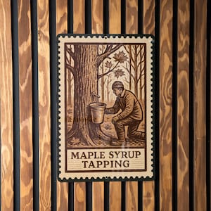 May include: A vintage-style sign depicting maple syrup tapping. The illustration shows a person collecting sap from a tree. The sign is framed with a postage stamp design and the words "MAPLE SYRUP TAPPING". The sign is mounted on a wooden slatted wall.