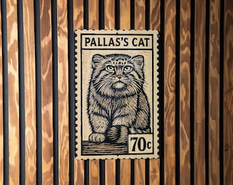 Op de afbeelding: Een rechthoekig bord met een gedetailleerde illustratie van een Pallas' kat, die op een postzegel lijkt. Het bord leest "PALLAS'S CAT" bovenaan en "70c" onderaan. Het is gemonteerd op een houten wand met verticale lamellen.