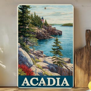 May include: A rectangular metal sign featuring a scenic coastal landscape with a lighthouse, rocky cliffs, and a body of water. The sign has the word "ACADIA" in white capital letters on a dark blue banner.