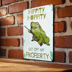 May include: A green frog holding a rifle with the text "Hippity Hoppity Get Off My Property" on a blue background.