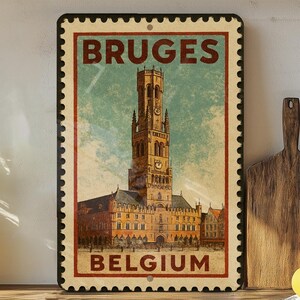 May include: Vintage-style metal sign featuring the word "BRUGES" at the top and "BELGIUM" at the bottom. The sign depicts a detailed illustration of a tall building with a clock tower, set against a sky background. The sign has a postage stamp design.