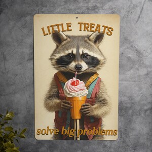 May include: A metal sign with a raccoon wearing a red and blue vest holding a milkshake with a cherry on top. The sign says "Little Treats Solve Big Problems".