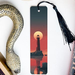 May include: A bookmark featuring a lighthouse scene at sunset, with a black tassel. The bookmark has a dark blue to red gradient background, with a lighthouse silhouetted against a large sun. A decorative snake and a book are also visible.