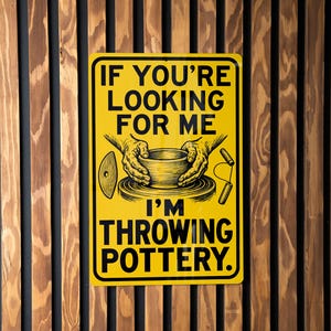 May include: A rectangular yellow metal sign with black text that reads IF YOU'RE LOOKING FOR ME I'M THROWING POTTERY. The sign features a black graphic illustration of two hands shaping a clay bowl on a pottery wheel, with a rib tool and wire cutter.