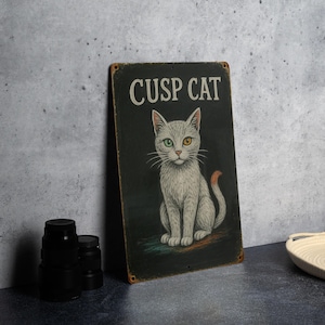 May include: A vintage-style metal sign with the text "CUSP CAT" above a seated cat illustration. The cat has gray fur, a green and yellow eye, and an orange tail. The sign has a black background and a distressed, rusty edge.