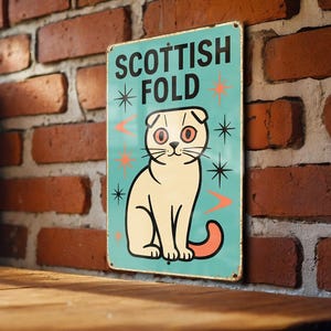 May include: A vintage-style metal sign featuring a cream-colored Scottish Fold cat illustration on a teal background. The sign reads "SCOTTISH FOLD" in black text with starburst and arrow accents. The sign is mounted on a brick wall.