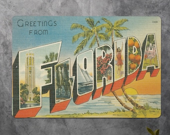 May include: Vintage postcard with the word "Florida" in large, colorful letters. The postcard features a scene of palm trees, a sunset, and a sailboat. The text "Greetings from" is at the top of the postcard.