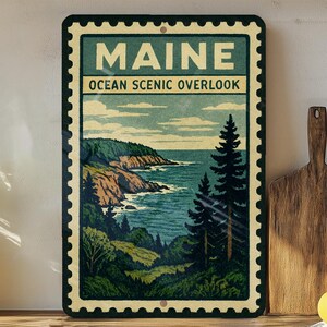 A framed vintage-style poster of Maine's oceanic scenery, featuring a coastal landscape with mountains, pine trees, and the ocean.