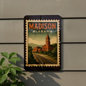 A framed vintage-style poster of a train station in Alabama, with a clock tower and train tracks, is displayed on a wall.