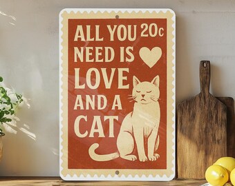 May include: A rectangular sign with a red background and a cream-colored border. The sign features the text "ALL YOU NEED IS LOVE AND A CAT" with a heart symbol and a drawing of a cat. The sign is a decorative item.