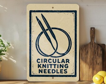 May include: A rectangular sign with a cream background and a dark blue border. The sign features an illustration of circular knitting needles and the words "CIRCULAR KNITTING NEEDLES" in dark blue. The sign is mounted on a wooden surface.