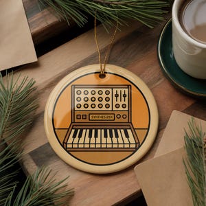 May include: A round, cream-colored ornament with a gold string for hanging. The ornament features a synthesizer design in shades of brown and black, with the word "SYNTHESIZER" printed below the keys. A festive holiday decoration.