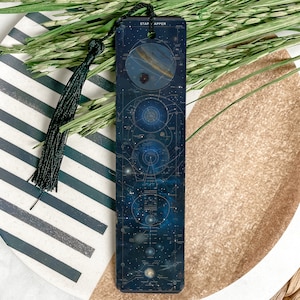 May include: A black bookmark with a blue and white illustration of the solar system and the text "Stargazer" on the top. The bookmark has a black tassel.