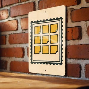 May include: A rectangular metal sign with a postage stamp design. The sign features nine yellow squares with a corner fold, set within a black border. The sign is mounted on a brick wall.