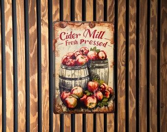 May include: A vintage-style metal sign with the text "Cider Mill - Fresh Pressed" in red and black lettering. The sign features a painting of two wooden barrels filled with red apples and green leaves.