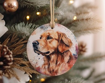 May include: A round ceramic ornament featuring a watercolor painting of a golden retriever dog. The dog's fur is a rich golden brown, and its eyes are a deep brown. The background is a soft watercolor wash of blues, pinks, and greens.