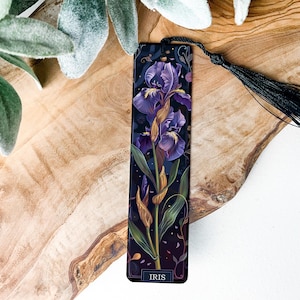 May include: A black bookmark with a purple and gold iris flower illustration. The bookmark has a black tassel and the text "IRIS" at the bottom.