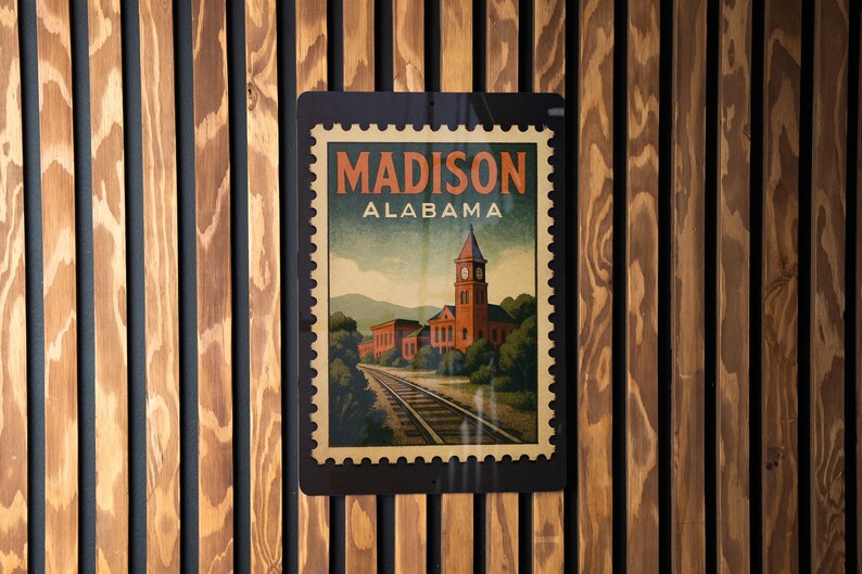 A vintage-style postage stamp from Alabama featuring a train track and a building, mounted on a wooden wall.