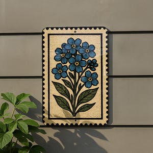 A decorative tile with a blue flower design is mounted on a wall, accompanied by a small green plant to the left.