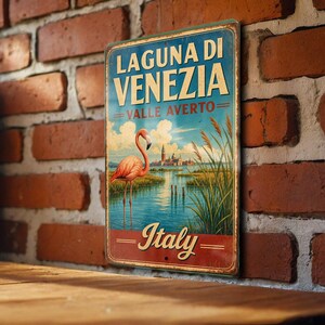 May include: Vintage metal sign featuring a flamingo in a lagoon with the text "Laguna di Venezia, Valle Averti, Italy." The sign has a distressed look with a blue sky, water, and a building in the background. The sign is mounted on a brick wall.