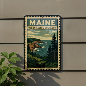 A framed vintage-style sign depicting a scenic coastal landscape with mountains, trees, and the ocean, mounted on a wall.