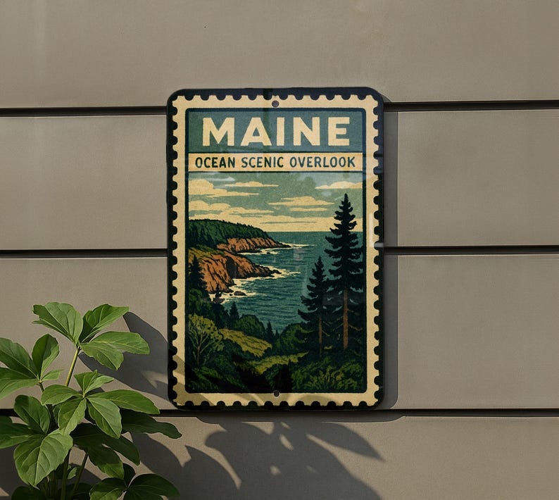 A framed vintage-style sign depicting a scenic coastal landscape with mountains, trees, and the ocean, mounted on a wall.