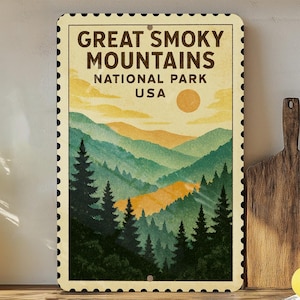 May include: A rectangular metal sign featuring a vintage-style illustration of the Great Smoky Mountains National Park in the USA. The artwork depicts layered green and yellow mountains, pine trees, and a setting sun. The sign has a decorative border.