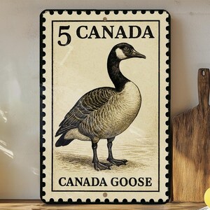 May include: A rectangular metal sign featuring a vintage illustration of a Canada Goose, resembling a postage stamp. The sign has a cream-colored background with the text "5 CANADA" at the top and "CANADA GOOSE" at the bottom, framed by a black border.