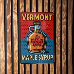 May include: A vintage-style metal sign with the words "VERMONT MAPLE SYRUP." The sign features a maple syrup bottle with a red maple leaf inside. The background is red with white dots and blue with white dots. The sign is mounted on a wooden slat wall.
