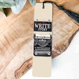 May include: A beige bookmark with a black and white image of a vintage typewriter. The typewriter has a sign above it that says "WRITE STORY".