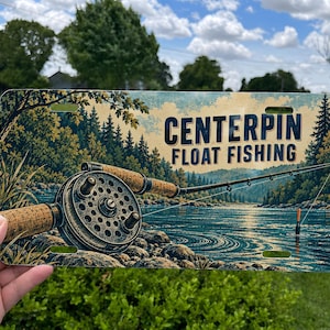 May include: A rectangular metal license plate featuring a vintage-style illustration of a fishing reel and rod over a river landscape with pine trees. The text "CENTERPIN FLOAT FISHING" is printed in dark blue capital letters on the right side.