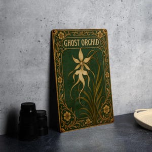 May include: A rectangular sign featuring a botanical illustration of a ghost orchid. The sign has a dark green background with gold floral accents and the words "GHOST ORCHID" in gold lettering. The orchid is white with long, flowing petals.
