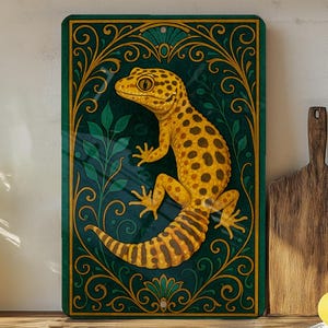 May include: A decorative rectangular sign featuring a yellow gecko with brown spots, set against a dark teal background with gold filigree and green leaf accents. The gecko is the focal point of the artwork.