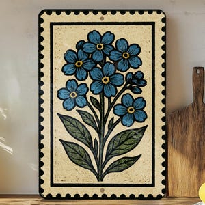 a decorative tile with a blue flower design, placed on a wooden surface next to a wooden cutting board and a potted plant.