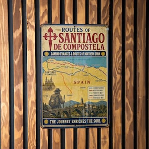 May include: A rectangular metal sign with the text "ROUTES OF SANTIAGO DE COMPOSTELA" and a map of Spain. The sign has a vintage aesthetic with a blue border and is mounted on a wooden wall.