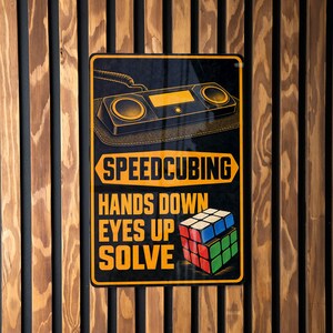May include: A rectangular metal sign with a black background featuring a graphic of a timer, the text SPEEDCUBING, the text HANDS DOWN EYES UP SOLVE, and a colorful 3x3 cube. The sign has a yellow border and yellow lettering throughout the design.