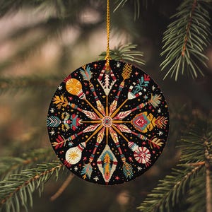 May include: A round Christmas ornament with a black background and a colorful mandala design featuring arrows, feathers, and stars.
