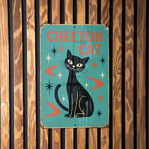 May include: A vintage-style metal sign featuring a black cat illustration with the text "CHEETOH CAT" in red. The sign has a teal background with star and boomerang accents, and is mounted on a wooden slat wall.