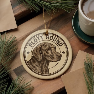 May include: Cream-colored ceramic ornament featuring a Plott Hound illustration. The dog's profile is in a sepia tone, encircled by the words "Plott Hound" and two stars. A gold string is attached for hanging. A perfect gift for dog lovers.