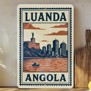 May include: A rectangular sign featuring a vintage-style illustration of Luanda, Angola. The design includes a cityscape, a boat on the water, and the text "LUANDA" and "ANGOLA" in a bold font. The sign has a cream-colored background with a dark blue border.