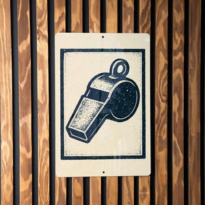 May include: A rectangular sign featuring a navy blue whistle illustration with a black border. The sign is mounted on a wooden wall with vertical brown and black planks.