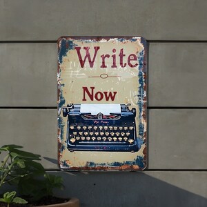 May include: A vintage-style metal sign with a distressed look. It features a black typewriter with a white paper insert and the words "Write Now" in red lettering.