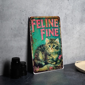 May include: A vintage-style metal sign with a distressed, rusty look. It features a cartoon cat with green eyes and a pink nose, and the text "Feline Fine" in pink letters on a teal background.