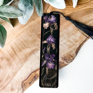 May include: Black bookmark with a purple and white iris flower design. The bookmark has a black tassel and the word "IRIS" printed at the bottom.