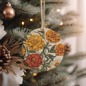 May include: A round, cream-colored Christmas ornament with a floral design. The ornament features a pattern of orange, yellow, and white marigolds on a cream background.