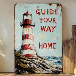 May include: A vintage-style metal sign with a red and white striped lighthouse, blue sky, and ocean waves. The sign reads "Guide Your Way Home".