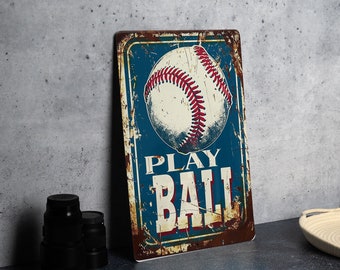 May include: A vintage-style metal sign with a distressed blue background and a white baseball with red stitching. The sign reads "PLAY BALL" in white letters.