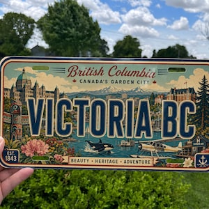 May include: A rectangular metal license plate featuring the text VICTORIA BC in large blue letters. The design includes illustrations of a totem pole, a seaplane, an orca, and the British Columbia Parliament Buildings with the text Canada's Garden City.